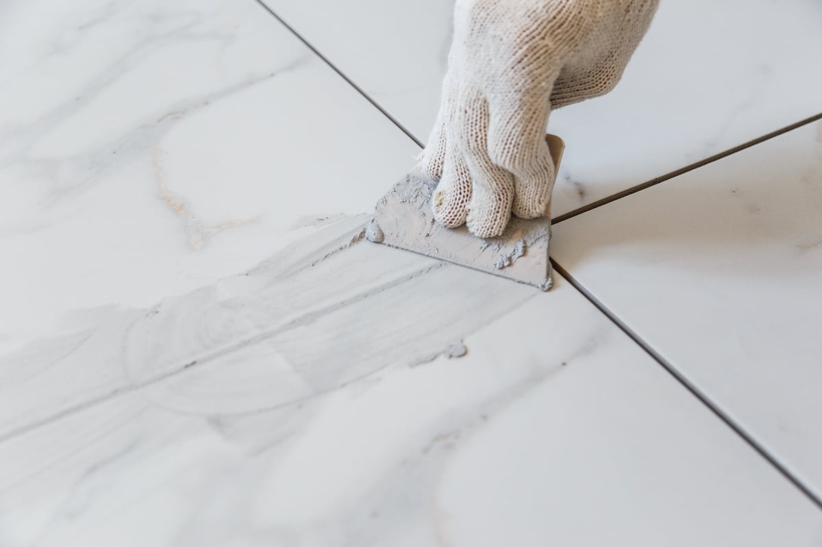 Tradesman grouting tile seams to re-secure loose tile on a floor