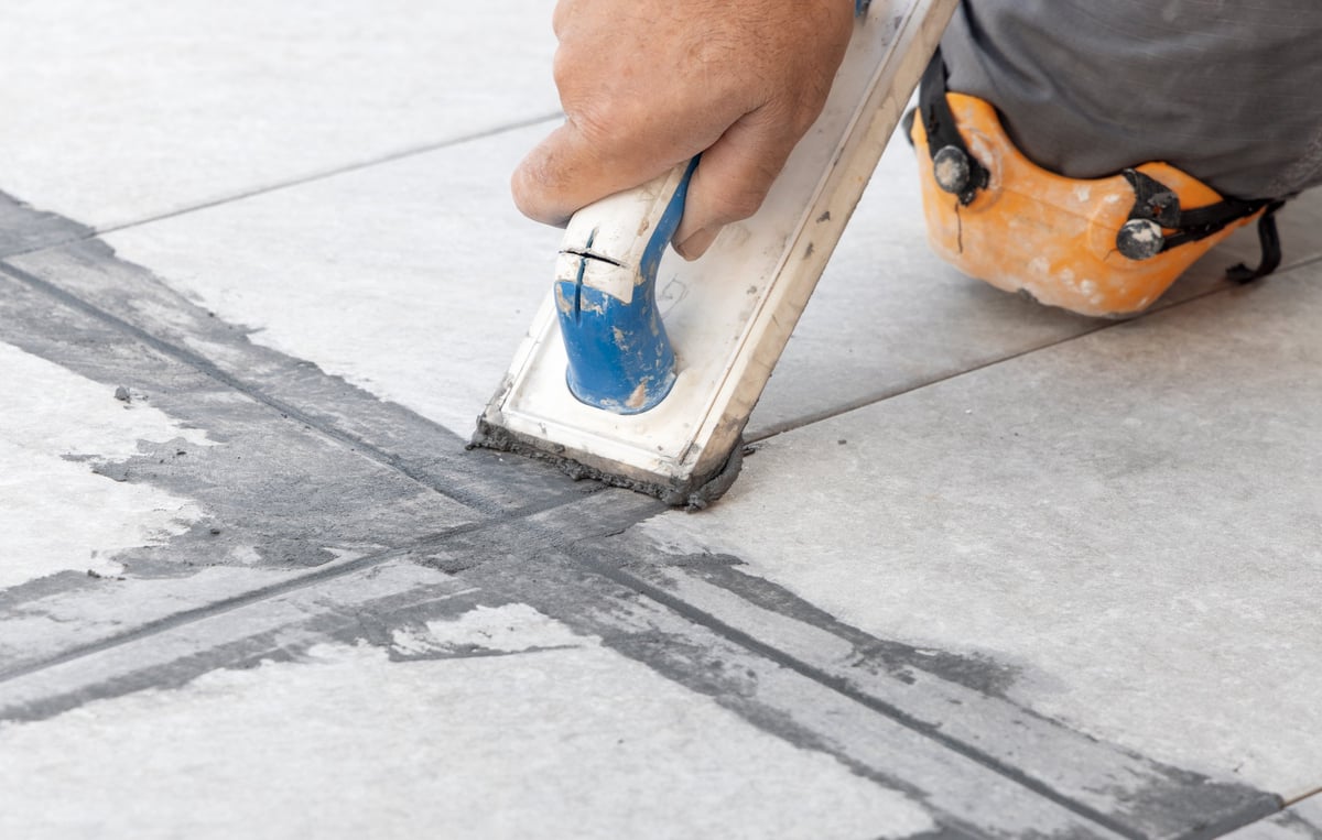 Craftsman repairing loose tile and re-grouting tile joints on a floor with a grout float