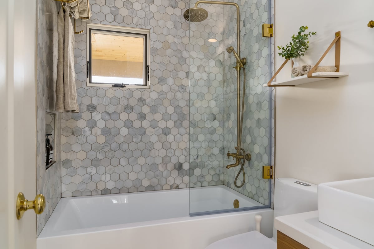 Modern white bathroom with hexagonal floor tile and gold fixtures after loose tile repair