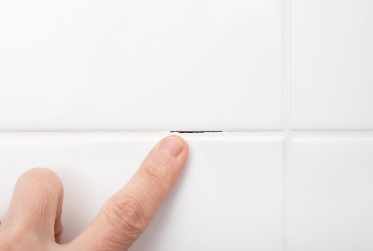White bathroom tile with a dark crack in the grout line showing failed grout repair